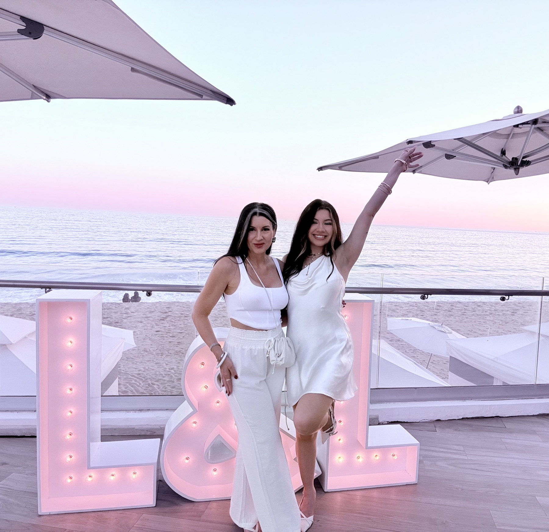 Two of our girls striking a pose at the L&L letters under a pink sky