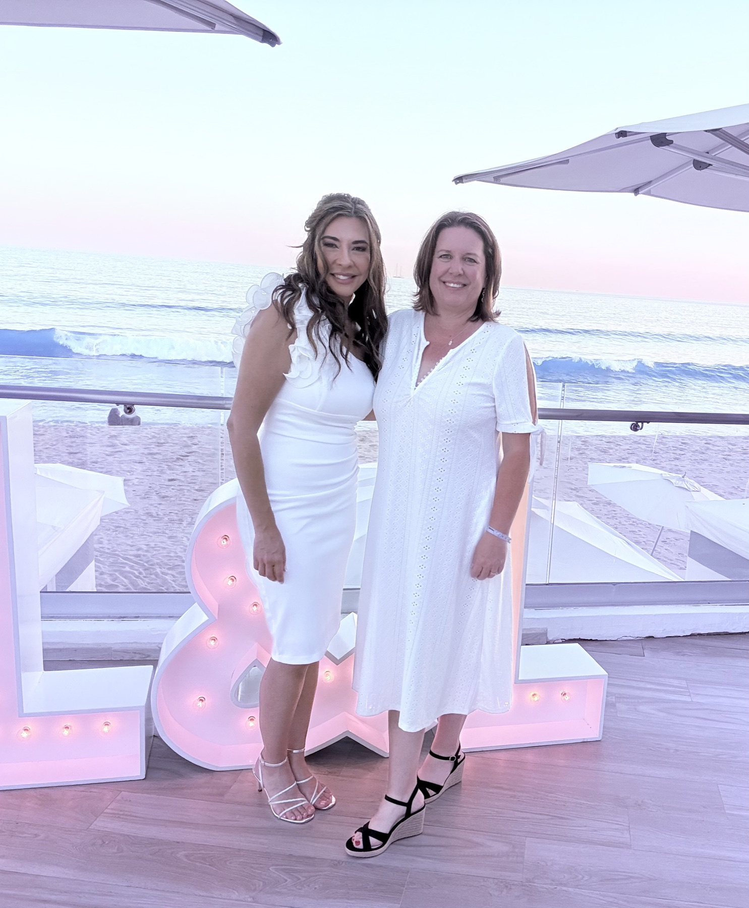 Two guests in white at the L&L letters over the beach
